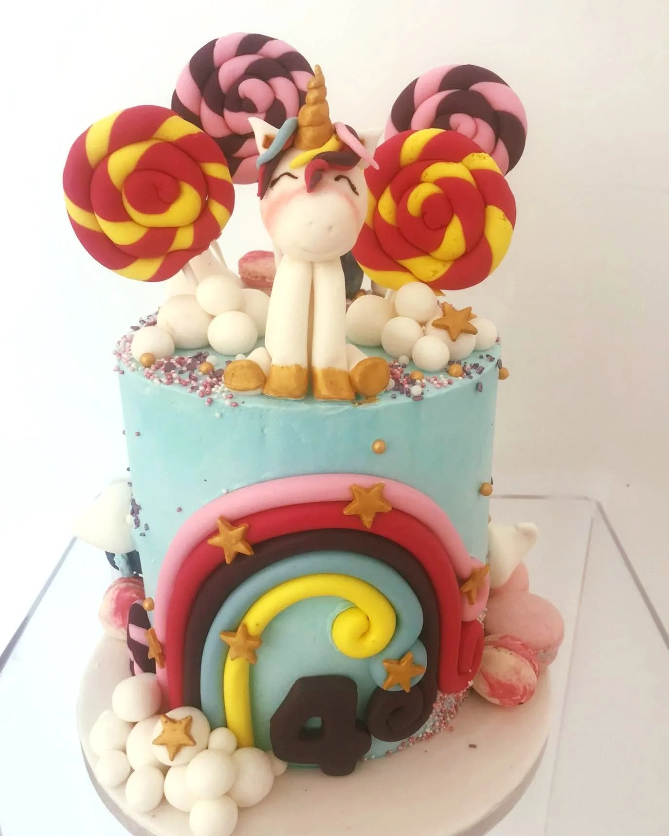Children's birthday cake with a hand-modelled unicorn, rainbow and lollipops in pastel sugarpaste