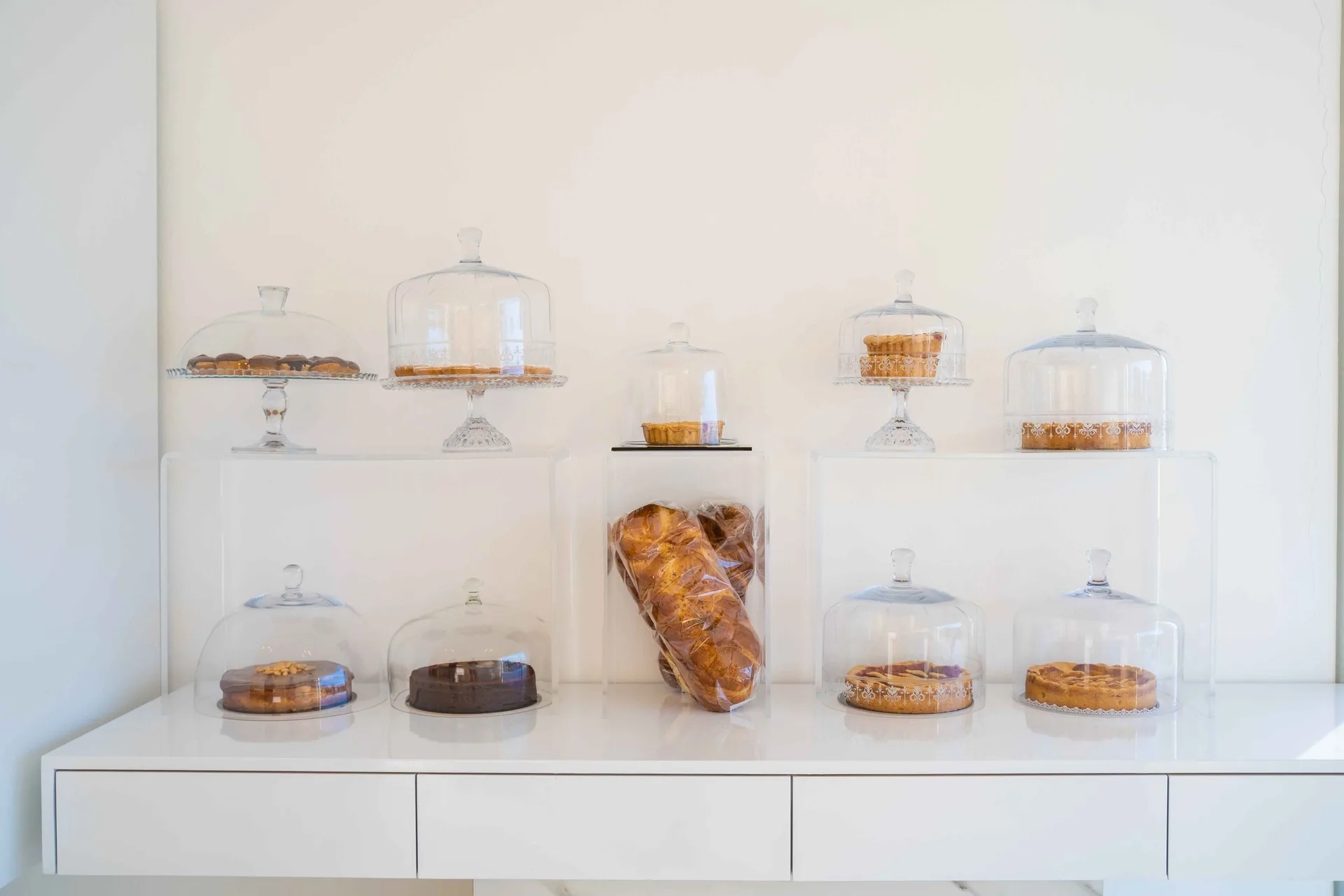 White patisserie counter with cakes and pastries under glass domes